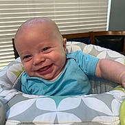 A.j. is registered to the contest to win money with this photo: baby, smiling, infant, blue_shirt, baby_seat, patterned_fabric, indoor, happy, child, face, head, person, furniture, home, window_blinds, wooden_chair, cute, closeup, comfort, young_child