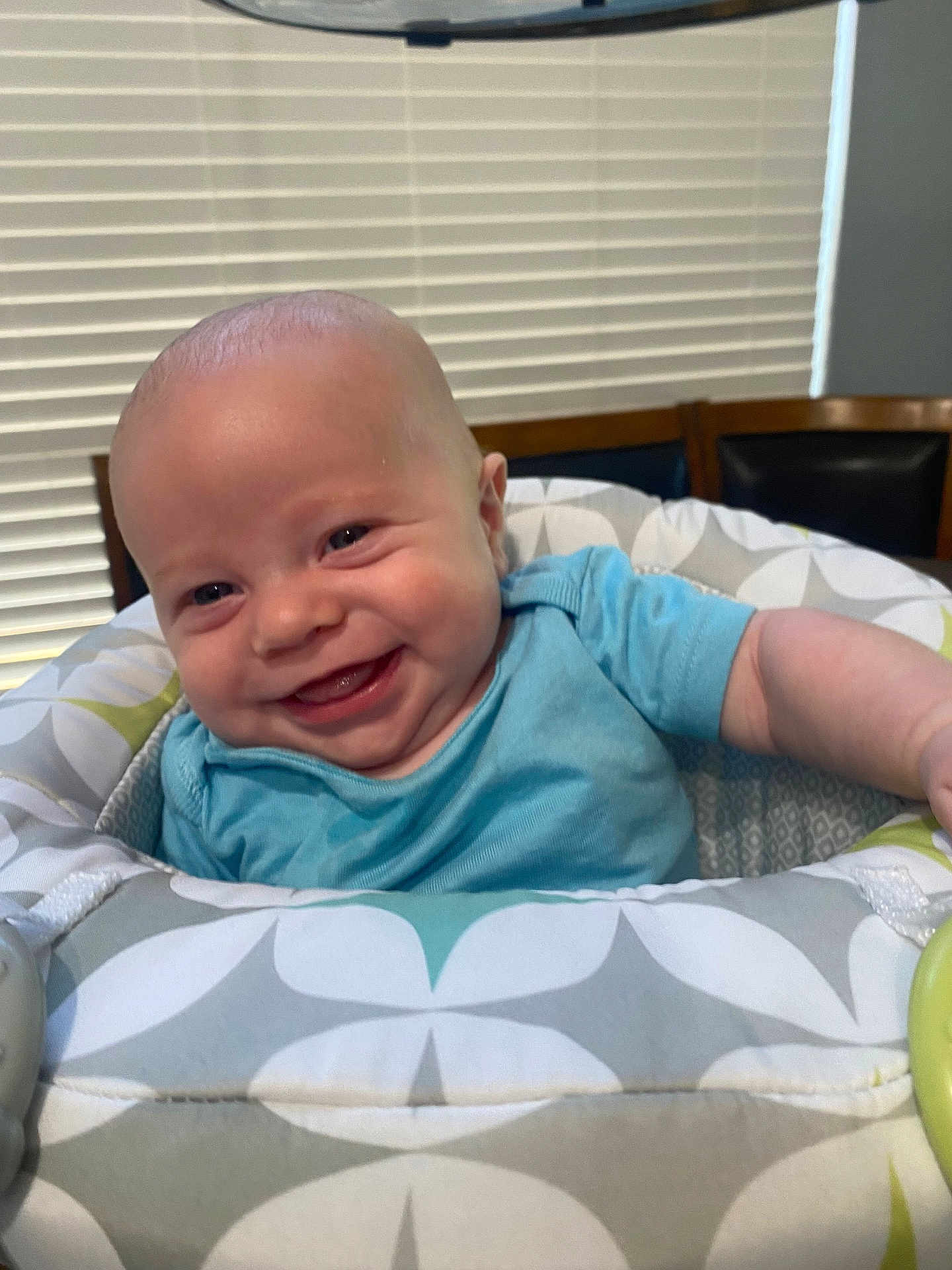 A.j. is registered to the contest to win money with this photo: baby, smiling, infant, blue_shirt, baby_seat, patterned_fabric, indoor, happy, child, face, head, person, furniture, home, window_blinds, wooden_chair, cute, closeup, comfort, young_child