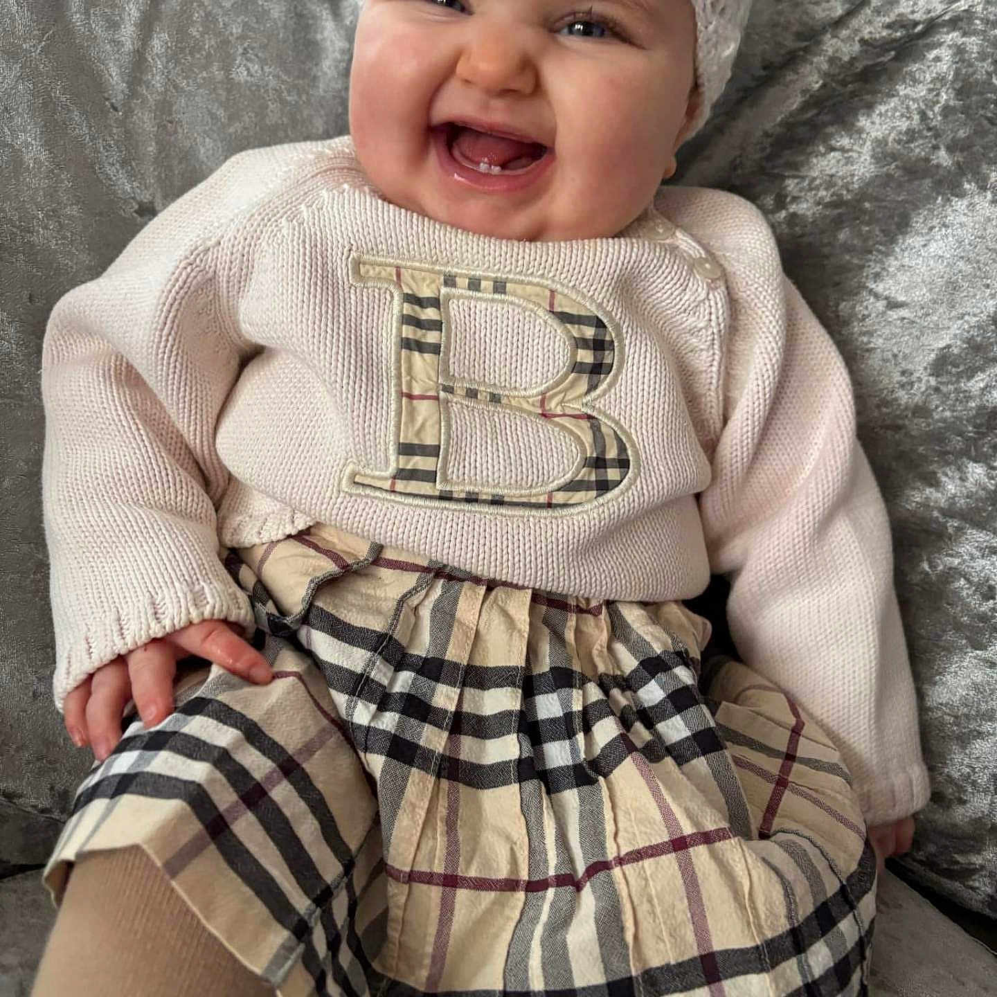 Darcey Leigh is registered to the contest to win money with this photo: baby, child, clothing, couch, cozy, cute, face, hand, happy, headband, indoor, knitwear, person, plaid_skirt, portrait, seated, smiling, soft_fabric, sweater, toddler