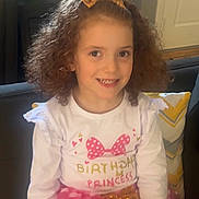 Luisa joined the competition — help win amazing prizes! child, girl, curly_hair, bow, birthday, princess, smile, white_shirt, pink_skirt, polka_dots, couch, pillow, indoor, portrait, happy, celebration, home, furniture, person, sitting