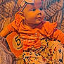 baby, infant, blue_eyes, headband, bow, orange_clothing, floral_pattern, milestone_card, 5_months, blanket, sitting, cute, child, portrait, indoors, soft_texture, foot, curious, person, smiling