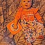 baby, infant, child, milestone_card, orange_clothing, floral_pants, headband, bow, blanket, texture, lying_down, blue_eyes, bare_feet, cute, portrait, indoors, person, smiling, early_childhood, colorful