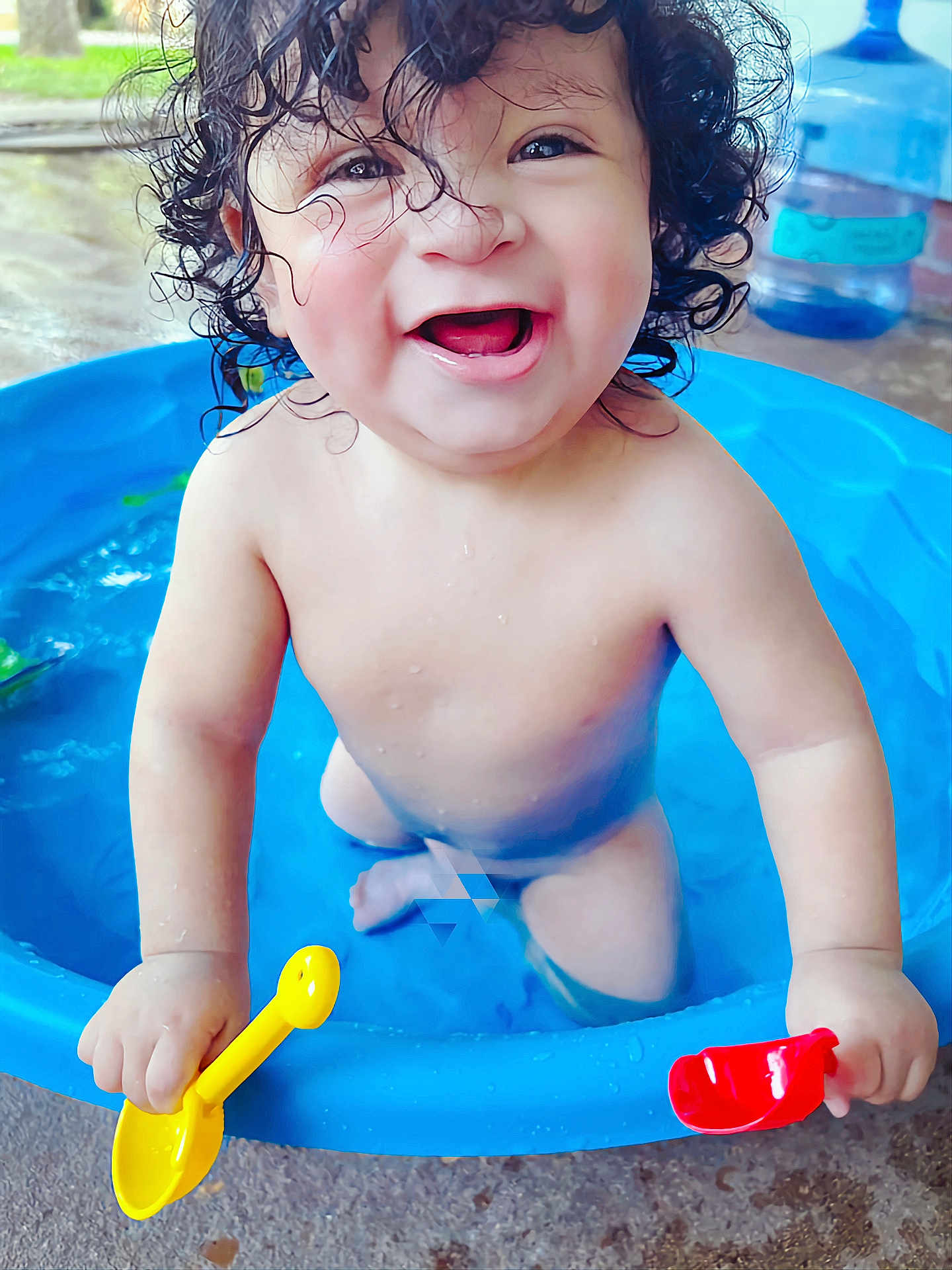 Obed is registered to the contest to win money with this photo: toddler, child, curly_hair, water, blue_pool, toy_shovel, yellow_shovel, red_shovel, smiling, happy, playtime, outdoor, water_droplets, bare_chest, splashing, summer, fun, cute, baby, expression
