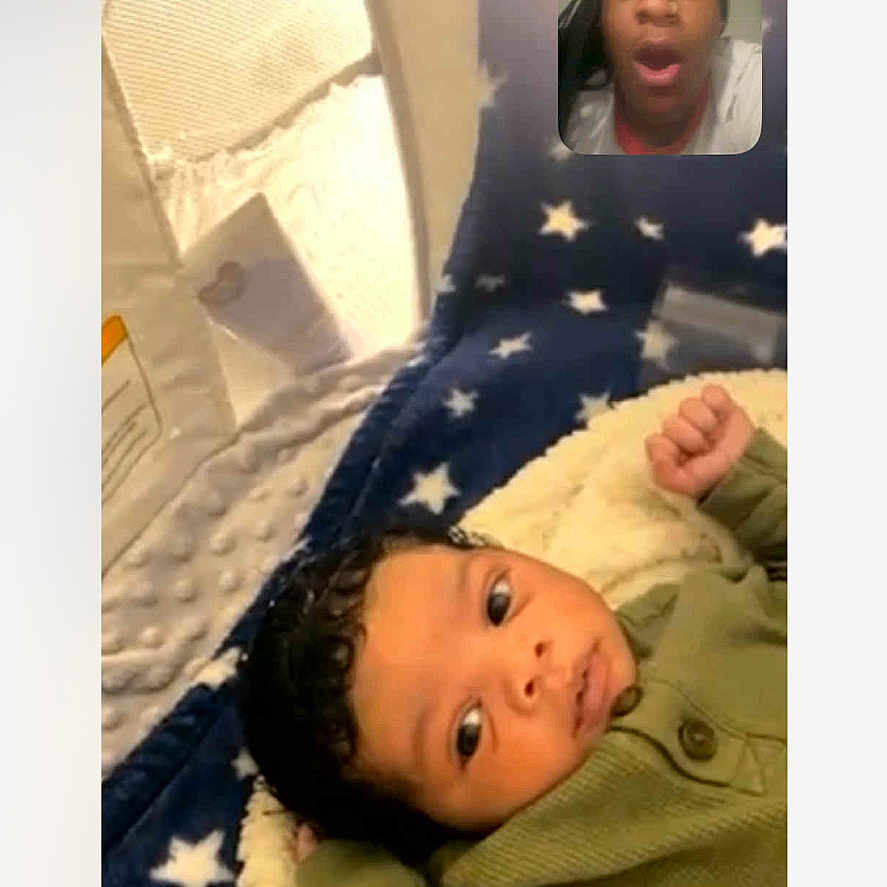 Tavon is registered to the contest to win money with this photo: baby, blanket, clothing, communication, curly_hair, expression, face, green_sweater, home, indoor, infant, lying_down, person, portrait, screen, soft_texture, stars, technology, video_call, yawning