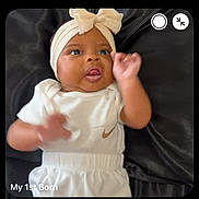 Jeriha is registered to the contest to win money with this photo: baby, infant, headband, bow, white_clothing, black_background, face, hand, lying_down, curious, expression, text_overlay, video_call, screenshot, person, portrait, indoor, cute, small_face, smiling_adult