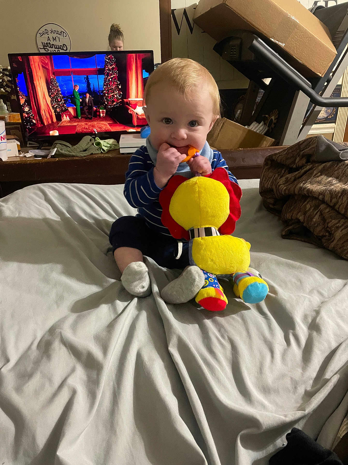 Weston joined the competition — help win amazing prizes! baby, child, toy, plush_toy, bed, blanket, person, indoor, television, woman, curious, chewing, blue_clothing, striped_shirt, sock, furniture, room, home, casual, young_child