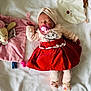 baby, sleeping, pacifier, red_skirt, cat_print, head_wrap, plush_toy, blanket, soft_texture, pink, beige, toddler, clothing, cute, infant, lying_down, cozy, child, toy, portrait
