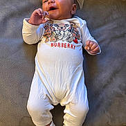 Royal is registered to the contest to win money with this photo: baby, bear_pattern, child, couch, cozy, cushion, face, fingers, hand, happy, home, indoor, infant, lying_down, onesie, photography, portrait, smiling, socks, white_outfit