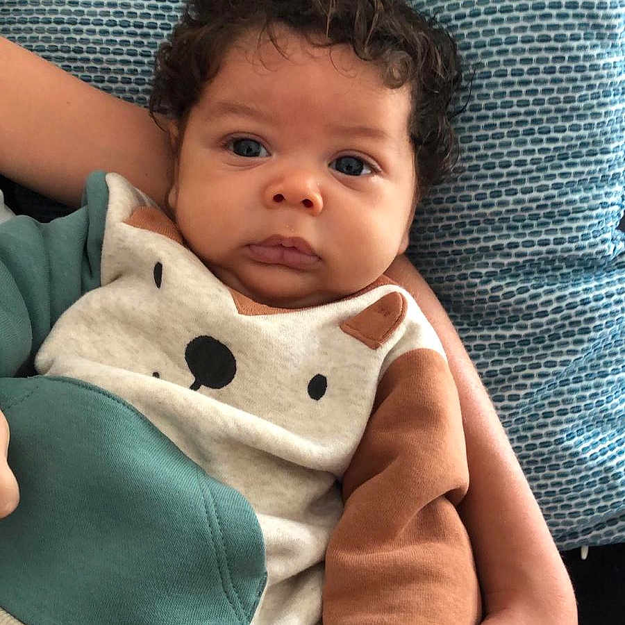 Eden a rejoint le concours — aidez-le/la à gagner de superbes lots ! baby, bear_design, blue_cushion, child, clothing, curly_hair, cute, face, hand, indoors, infant, person, portrait, resting, sitting, skin, sleeve, textile, warm_clothing, young_child