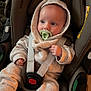 baby, car_seat, pacifier, hoodie, infant, child, seatbelt, clothing, blue_socks, indoor, cute, young_child, sitting, safety, person, portrait, face, headwear, fabric, relaxing