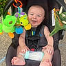 Graysen is registered to the contest to win money with this photo: baby, car_seat, bottle, toy, plush_toy, smiling, child, outdoor, grass, concrete, happy, infant, seatbelt, cute, person, foot, hand, summer, playful, colorful