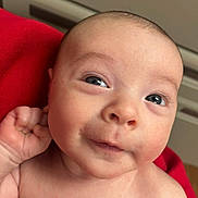 Graysen is registered to the contest to win money with this photo: baby, closeup, curious, cute, expression, eyes, face, hand, head, human, indoors, infant, newborn, person, portrait, red_cloth, skin, smile, soft_skin, young_child