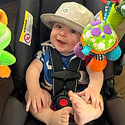 Graysen is registered to the contest to win money with this photo: baby, child, car_seat, hat, smile, toy, colorful, indoors, seatbelt, infant, playful, foot, hand, happy, closeup, cute, childrens_toy, soft_toy, fabric, portrait