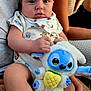 baby, infant, plush_toy, stuffed_animal, onesie, bib, hand, lap, person, clothing, face, expression, blue, pineapple, cute, indoor, family, child, holding, sitting