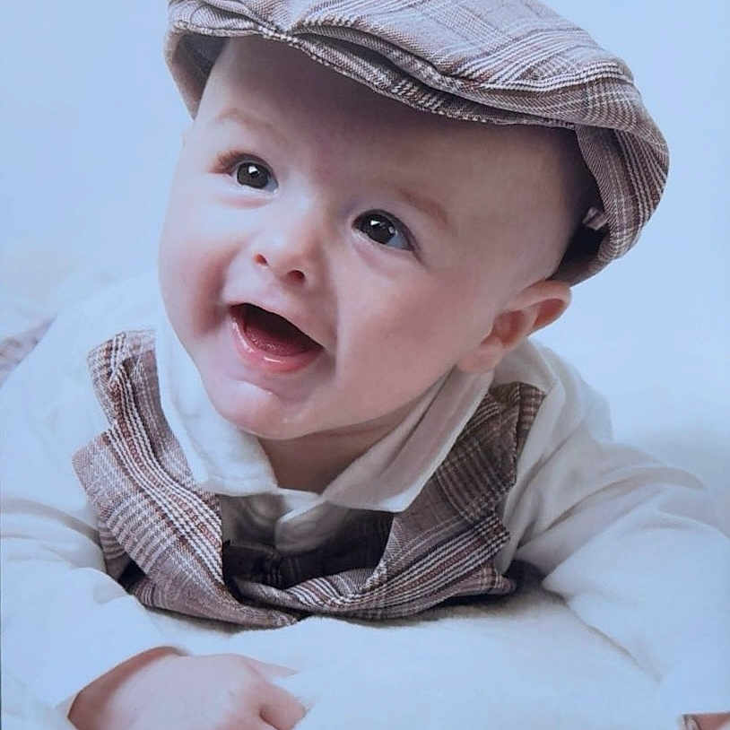 Tommy-Lee is registered to the contest to win money with this photo: baby, bright, cap, child, closeup, clothing, cute, face, happy, headwear, indoor, infant, lying_down, plaid, portrait, smile, soft_texture, vest, white_blanket, young