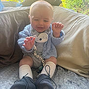 Tommy-Lee joined the competition — help win amazing prizes! baby, child, indoors, blue_sweater, striped_romper, white_socks, black_shoes, blanket, couch, window, greenery, happy, smiling, cute, person, infant, soft_light, home, comfort, toy
