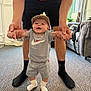 Tommy-Lee joined the competition — help win amazing prizes! baby, child, indoor, carpet, smiling, cap, shorts, socks, hands, standing, person, adult, support, nike, clothing, happy, footwear, home, living_room, cute