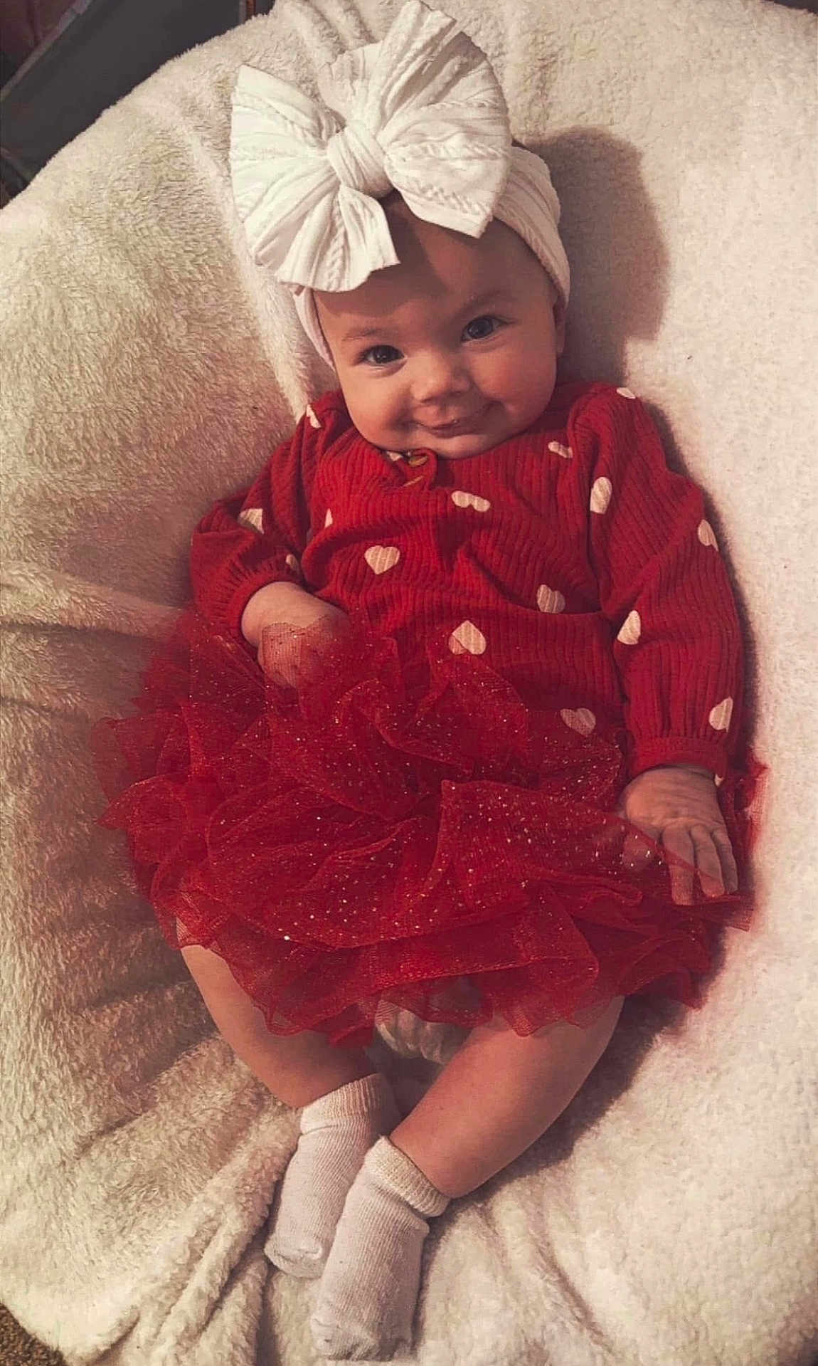 Layla joined the competition — help win amazing prizes! baby, infant, child, red_dress, tutu_skirt, headband, bow, socks, blanket, smile, cute, portrait, indoors, soft_texture, happy, sitting, face, person, clothing, cozy