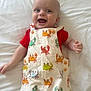 baby, infant, smiling, happy, cute, clothing, romper, crab_pattern, red_shirt, bed, white_bedspread, lying_down, cheerful, child, person, skin, face, hand, blue_eyes, short_hair