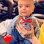 Atticus is registered to the contest to win money with this photo: baby, infant, cute, graduation_cap, toddler, suspenders, bow_tie, tattoo, hand, jeans, socks, indoor, person, clothing, seated, table, chair, blurred_background, heart_emoji, holding