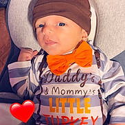 Atticus is registered to the contest to win money with this photo: baby, infant, hat, bow_tie, orange, clothing, cute, portrait, face, blue_eyes, hand, cushion, seat, striped, text_on_clothing, heart_emoji, indoor, soft_toys, child, cozy