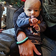 Louna participe au concours pour gagner de l'argent avec cette photo : baby, pacifier, beaded_necklace, adult_hand, bracelet, christmas_tree, ornaments, holiday, cozy, indoor, clothing, person, cute, holding, seated, face, expression, warm, decorations, festive