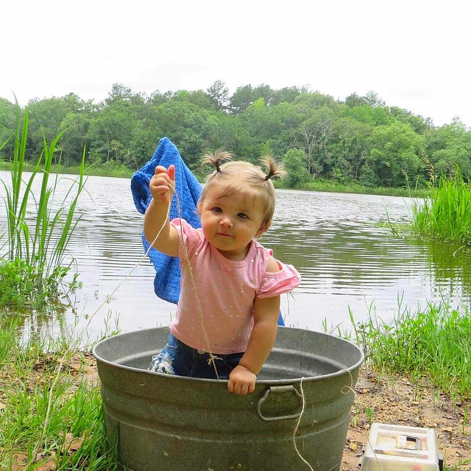 Mylee is registered to the contest to win money with this photo: baby, baby_toddler_clothing, bucket, fun, grass, happy, hat, lake, leisure, people_in_nature, photograph, plant, recreation, sitting, sky, soil, tire, toddler, tree, water