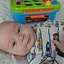 baby, infant, toy, colorful, plastic, workbench, onesie, car_pattern, blanket, face, child, lying_down, curious_eyes, indoor, playtime, early_childhood, cute, baby_clothes, soft_lighting, background