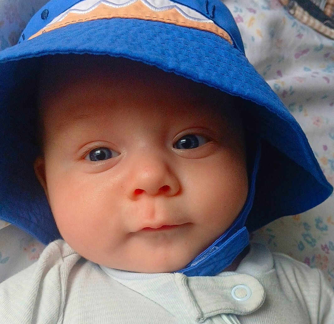 Corbin is registered to the contest to win money with this photo: baby, infant, face, blue_hat, bucket_hat, eyes, skin, clothing, portrait, closeup, child, cute, expression, headwear, newborn, person, lying_down, blanket, soft_light, indoors