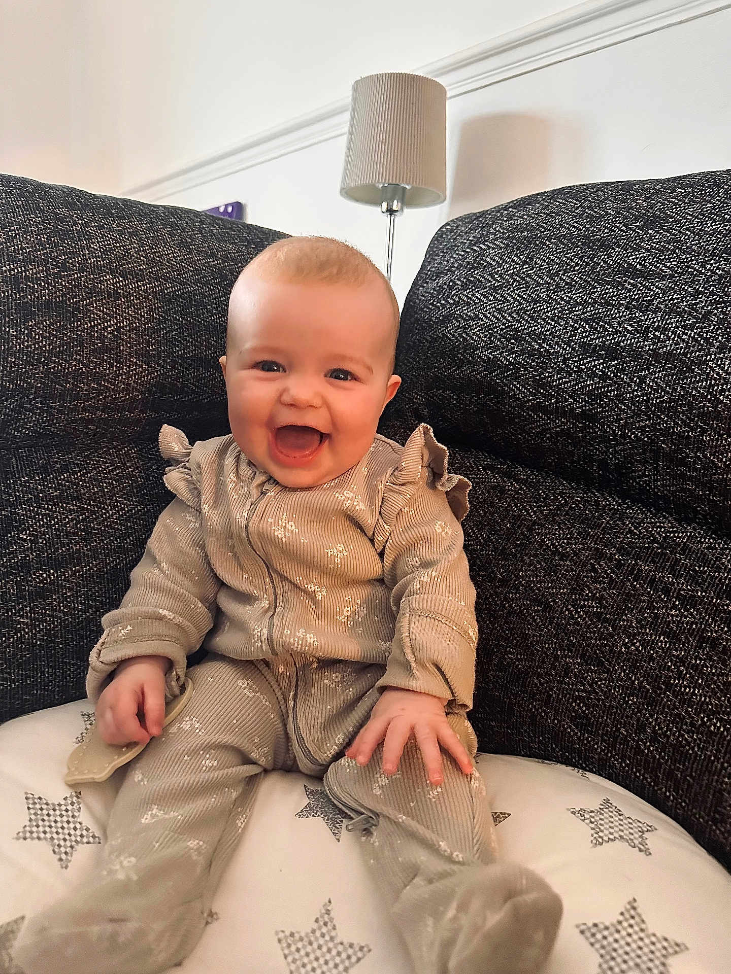 Elsie is registered to the contest to win money with this photo: baby, child, smiling, couch, cushion, lamp, indoor, happy, infant, clothing, seat, portrait, furniture, cozy, star_pattern, ruffles, young_child, light, home, comfort