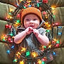 baby, child, infant, hat, bear_ears, vest, christmas_lights, holiday, festive, smiling, cute, colorful_lights, small_trees, quilted_background, indoor, portrait, happy, hands, warm_clothing, celebration