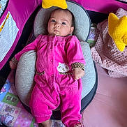 Zara is registered to the contest to win money with this photo: baby, infant, onesie, pink_clothing, baby_seat, cushion, playpen, yellow_star_toy, blanket, soft_toys, indoor, child, cute, face, feet, looking_up, comfort, resting, patterned_blanket, colorful