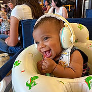 Shon is registered to the contest to win money with this photo: baby, headphones, smiling, infant, dinosaur, inflatable, seat, people, indoor, casual, joyful, child, cute, happy, clothing, table, can, background, woman, fun
