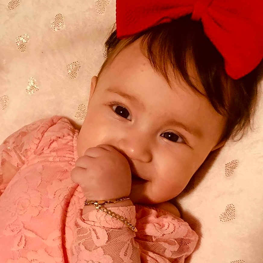 Salayah is registered to the contest to win money with this photo: adorable, baby, blanket, bracelet, child, closeup, cute, face, female, happy, heart_pattern, infant, pink_lace, portrait, red_bow, resting, smiling, soft_lighting, thumb_sucking, young