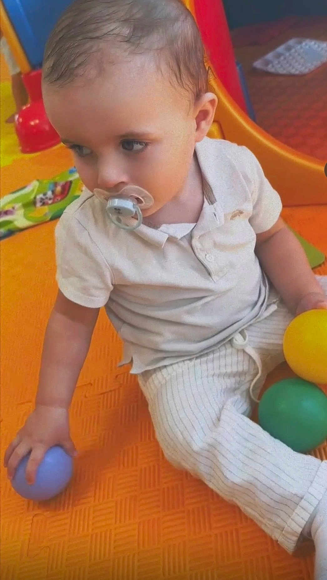 Kayden a rejoint le concours — aidez-le/la à gagner de superbes lots ! toddler, child, pacifier, ball, play_mat, indoor_playground, toy, orange_mat, white_clothing, striped_pants, sitting, cute, playtime, young_child, baby, colorful, hand, skin, face, short_hair