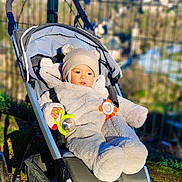 Thomas a rejoint le concours — aidez-le/la à gagner de superbes lots ! baby, stroller, outdoor, toy, child, fence, hat, plush_suit, winter_clothing, sunlight, grass, face, person, infant, seat, plaything, nature, daylight, relaxing, park