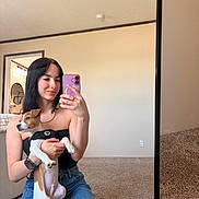 Nico is registered to the contest to win money with this photo: black_hair, carpet, casual_clothing, denim_skirt, dog, doorway, harness, holding, indoor, mirror, mirror_reflection, pet, seated, selfie, smartphone, smile, tattoo, technology, wall, woman