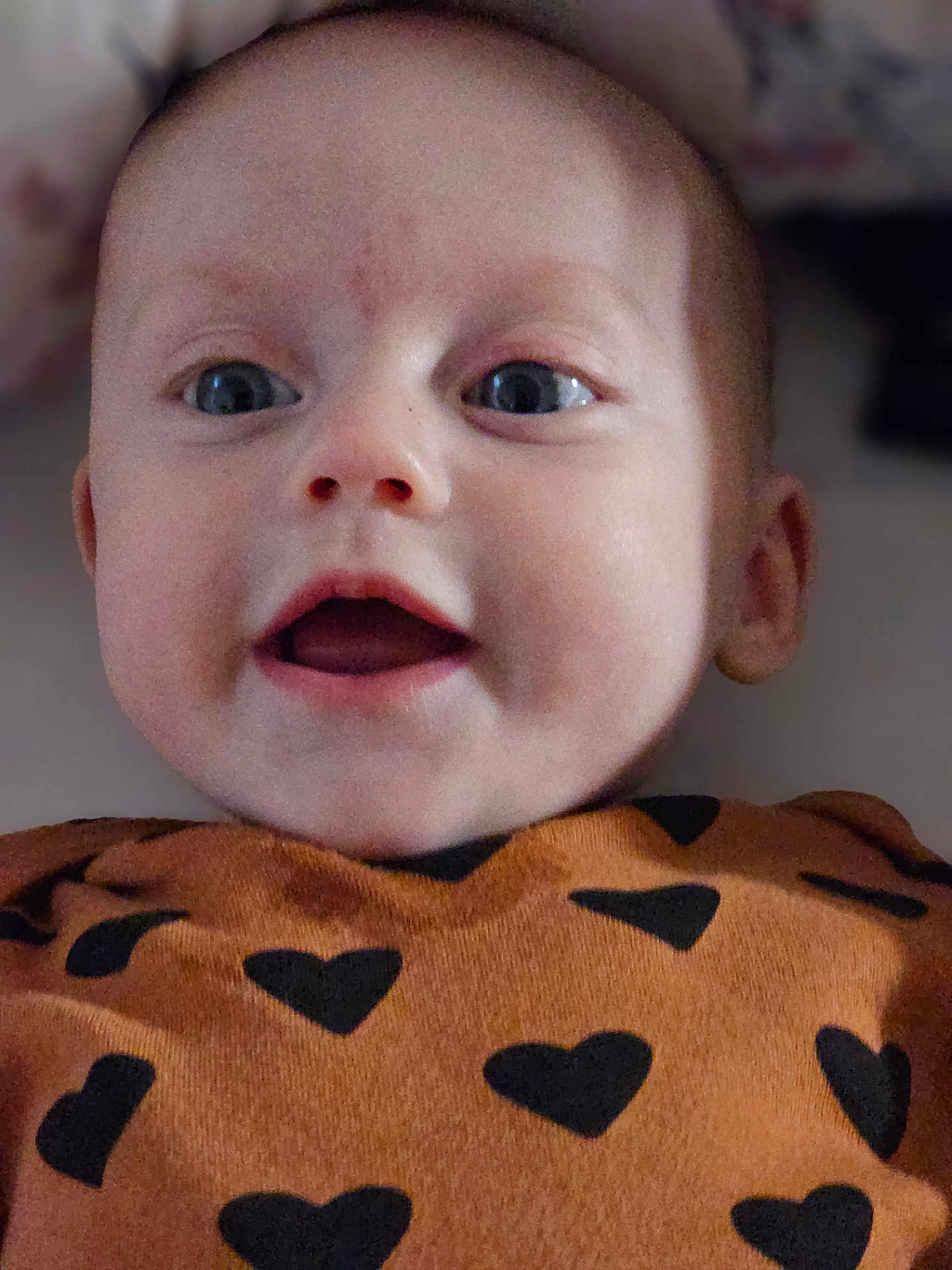 Aurora is registered to the contest to win money with this photo: baby, closeup, face, eyes, mouth, expression, infant, child, clothing, heart_pattern, cute, adorable, portrait, skin, head, young, person, happy, smiling, indoors