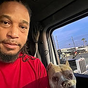 Channel joined the competition — help win amazing prizes! man, dog, vehicle_interior, window, truck, portrait, dreadlocks, red_shirt, pet, companion, daylight, outdoor_view, rest_stop, transport, face, animal, canine, friendship, candid, driver