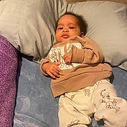 Jace is registered to the contest to win money with this photo: baby, infant, pajamas, sweater, bed, pillow, blanket, sleepwear, child, cute, indoors, resting, portrait, cozy, animal_print, soft_furnishing, comfort, young_child, relaxed, looking