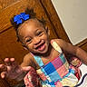 child, toddler, girl, smiling, happy, portrait, high_chair, colorful_dress, blue_bow, curly_hair, reaching, indoor, wooden_door, wall, toy, baby, sitting, face, laughter, family_photo