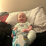 Paul is registered to the contest to win money with this photo: baby, infant, smiling, pillow, bed, blanket, clothing, socks, wipes, person, indoor, happy, relaxed, casual, couch, fabric, head, face, comfort, resting