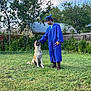 Duke joined the competition — help win amazing prizes! graduate, graduation_gown, cap, dog, pet, grass, outdoor, greenery, tree, fence, person, happy, smiling, yard, summer, blue, nature, animal, friendship, celebration