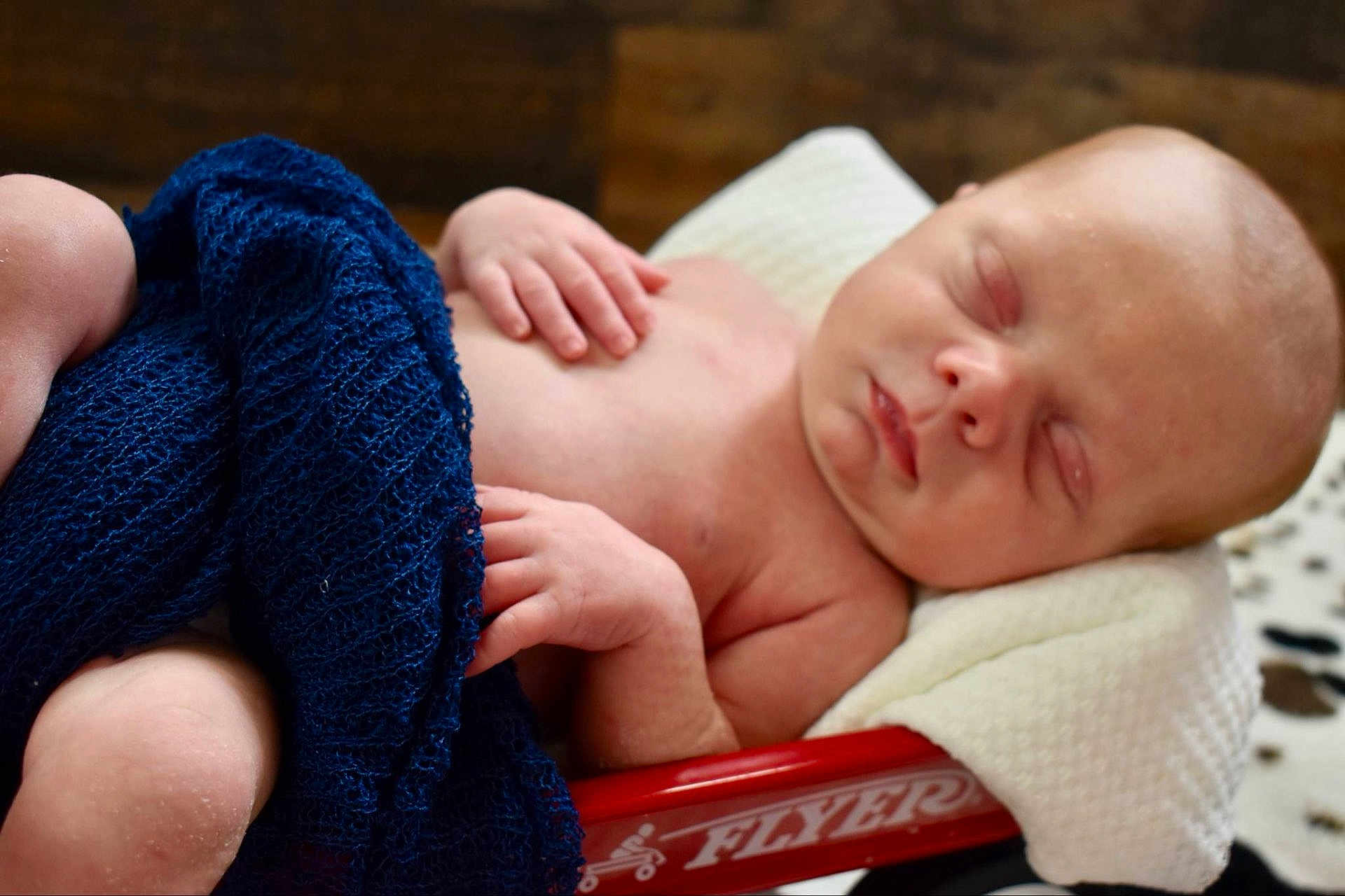 Carter is registered to the contest to win money with this photo: baby, newborn, sleeping, blanket, cloth, wagon, red_wagon, hand, skin, face, infant, rest, comfort, soft, cozy, indoors, closeup, portrait, peaceful, child