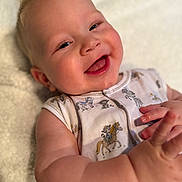 Kohen joined the competition — help win amazing prizes! adorable, baby, blanket, cartoon_print, child, closeup, cute, expression, face, hands, happy, indoors, infant, lying_down, mohawk, onesie, playful, skin, smiling, soft_texture