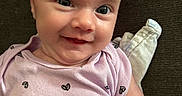 Micah is registered to the contest to win money with this photo: baby, infant, smile, face, eyes, onesie, purple_clothing, blanket, lying_down, cute, child, skin, head, expression, portrait, indoors, happy, person, newborn, closeup