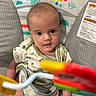 baby, infant, child, bouncer, toy, colorful, face, eyes, clothing, pattern, seat, indoor, cute, young, expression, hand, fabric, playful, animal_print, focus