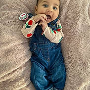 Aicha participe au concours pour gagner de l'argent avec cette photo : baby, blanket, blue_eyes, child, clothing, cute, denim_overalls, face, hands, happy, indoor, infant, lying_down, pacifier, person, playful, portrait, smiling, socks, soft_texture