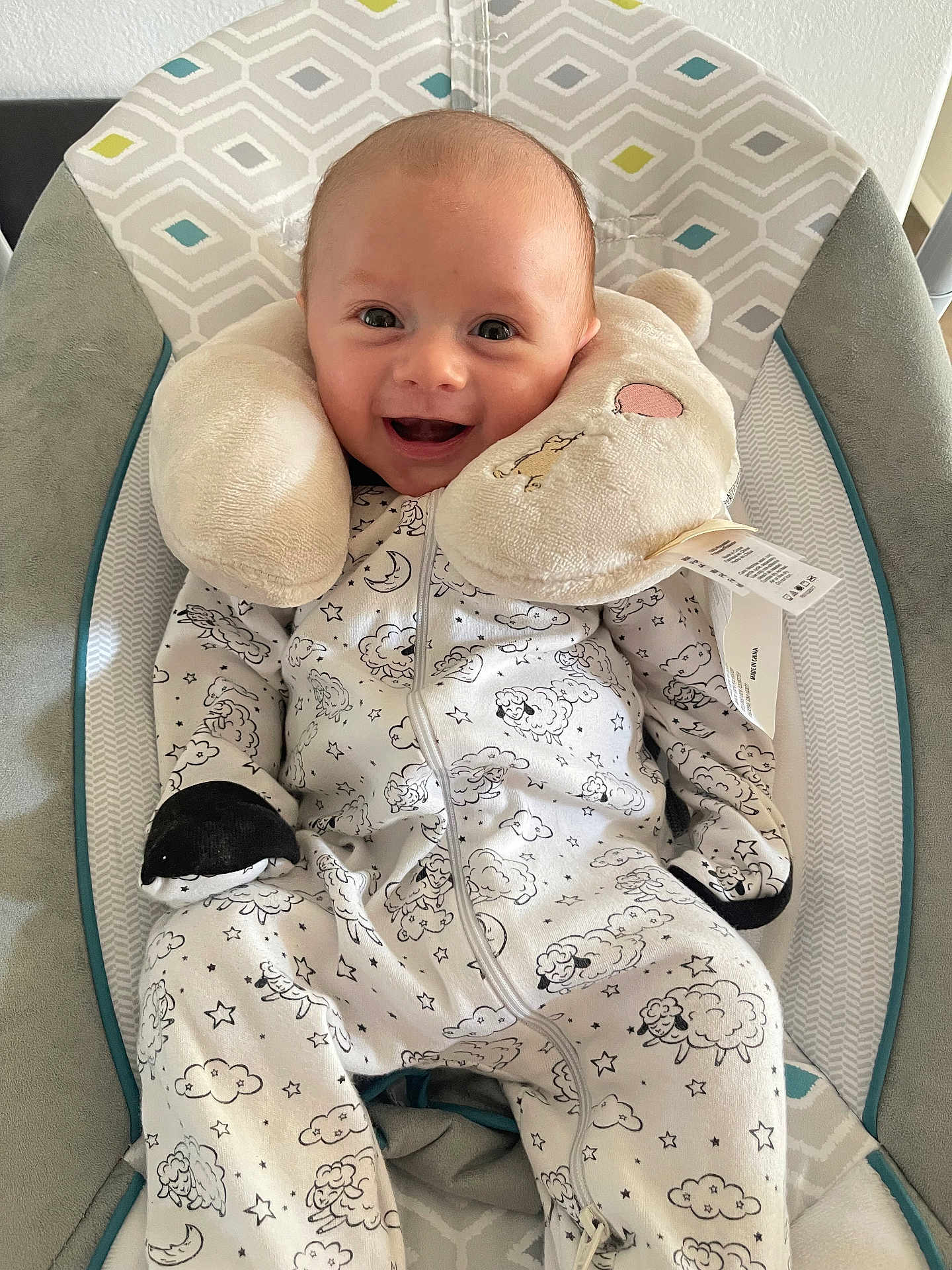 Micah is registered to the contest to win money with this photo: baby, smile, onesie, plush, baby_chair, cushion, happy, infant, face, comfort, sleeping_pillow, pattern, clothing, cute, child, indoors, soft_toy, relaxation, small_person, seated