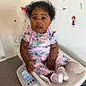 baby, child, infant, digital_scale, clothing, socks, curly_hair, wall_stickers, indoor, cute, sitting, looking_at_camera, table_surface, pink_outfit, measurement, expression, person, room, healthcare, portrait